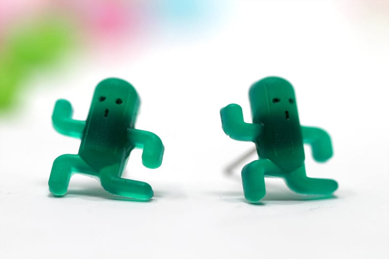May include: A pair of green plastic earrings shaped like running figures. Each figure has a simple face with two eyes and a mouth.
