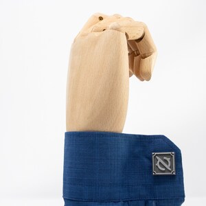 May include: A pair of silver cufflinks with a stylized letter 'N' design. The cufflinks are worn on a blue dress shirt.