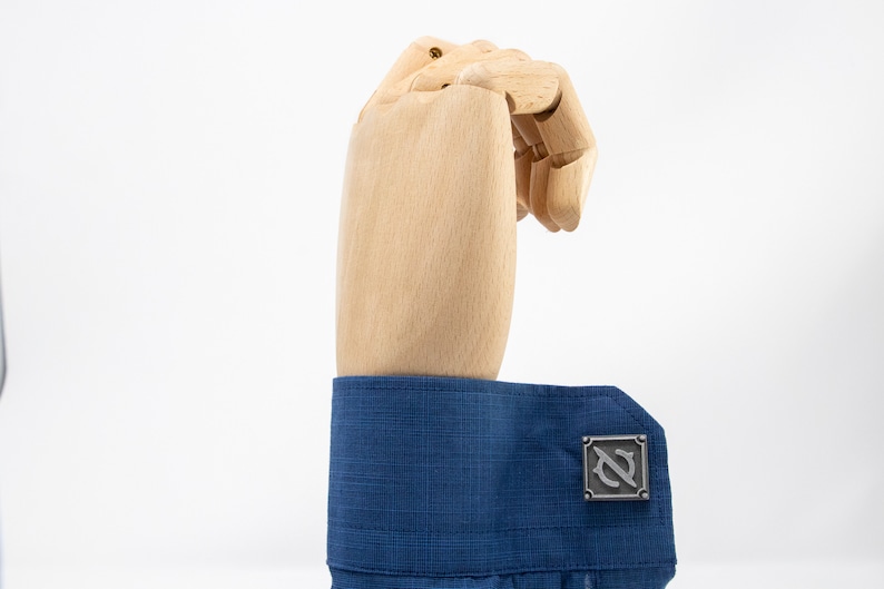 May include: A pair of silver cufflinks with a stylized letter 'N' design. The cufflinks are worn on a blue dress shirt.