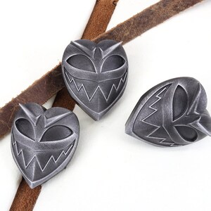 May include: Three silver heart-shaped pins with a menacing cartoon face design. The pins have a black and silver color scheme.