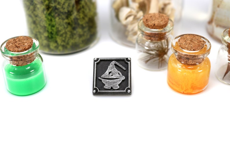 May include: A silver metal pin with a black background featuring a stylized image of a potion bottle with a cork stopper.