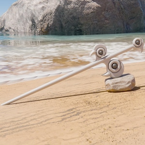 May include: A white metal decorative sword with a unique design, resting on a rock on a sandy beach.