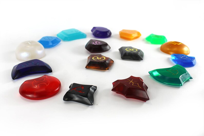 May include: A set of 14 colorful, translucent, and opaque gemstone-shaped game pieces with various symbols and designs. The pieces are arranged in a circle on a white background.