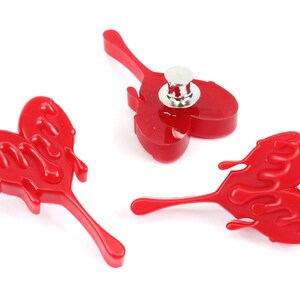 May include: Three red plastic heart-shaped pins with a dripping effect. The pins have a silver metal back with a pin mechanism.