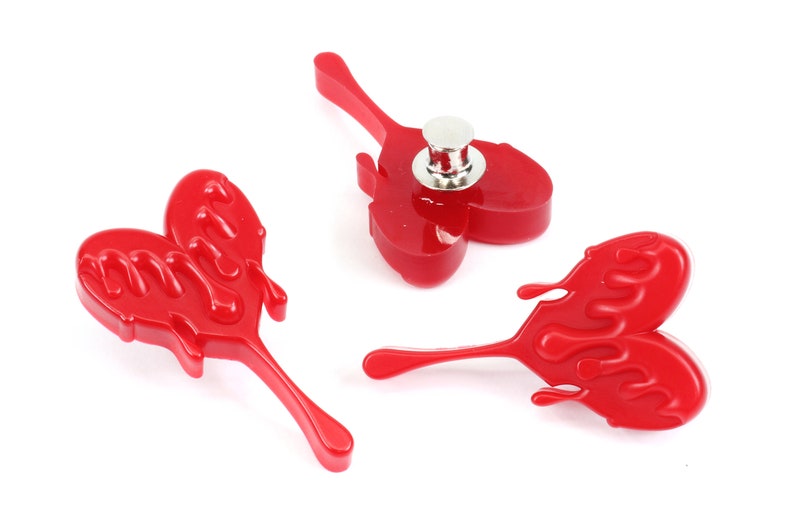May include: Three red plastic heart-shaped pins with a dripping effect. The pins have a silver metal back with a pin mechanism.