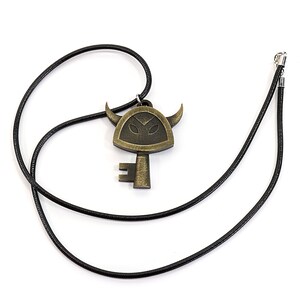 May include: A black cord necklace with a gold-toned key pendant featuring a stylized horned face.