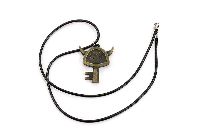 May include: A black cord necklace with a gold-toned key pendant featuring a stylized horned face.