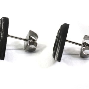 May include: A pair of black stud earrings with a geometric design. The earrings have a silver post and butterfly backing.