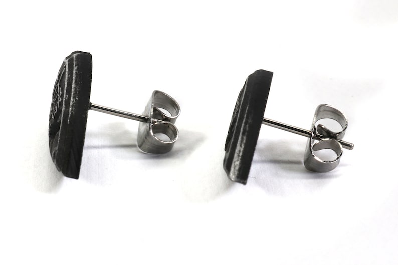 May include: A pair of black stud earrings with a geometric design. The earrings have a silver post and butterfly backing.