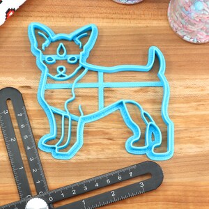 Puede incluir: Cortador de galletas de pl&aacute;stico azul con forma de perro peque&ntilde;o de pie sobre sus cuatro patas. El cortador de galletas est&aacute; sobre una superficie de madera.
