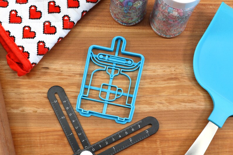 May include: Blue plastic cookie cutter shaped like a coffee maker. The cutter has a handle on top and a cup of coffee inside.