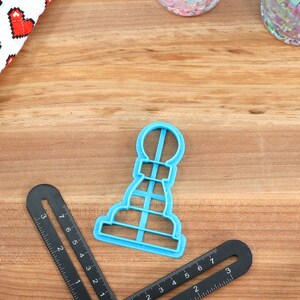 May include: A blue plastic cookie cutter shaped like a chess pawn on a wooden surface.