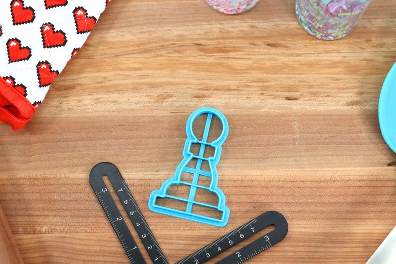 May include: A blue plastic cookie cutter shaped like a chess pawn on a wooden surface.