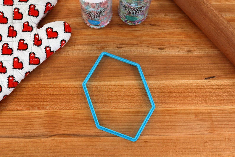 Op de afbeelding: Een blauwe, zeshoekige koekjesuitsteker van plastic op een houten oppervlak.