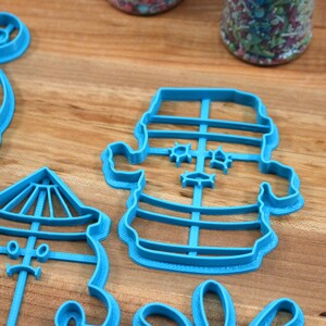May include: A set of four blue plastic cookie cutters shaped like a snowman, a carousel, a lighthouse, and a Christmas tree. The cutters are on a wooden surface.