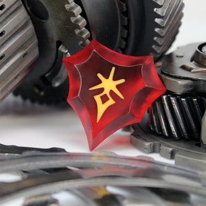 May include: A red, star-shaped, plastic token with a yellow Chinese character on it. The token is lying on a pile of metal gears.