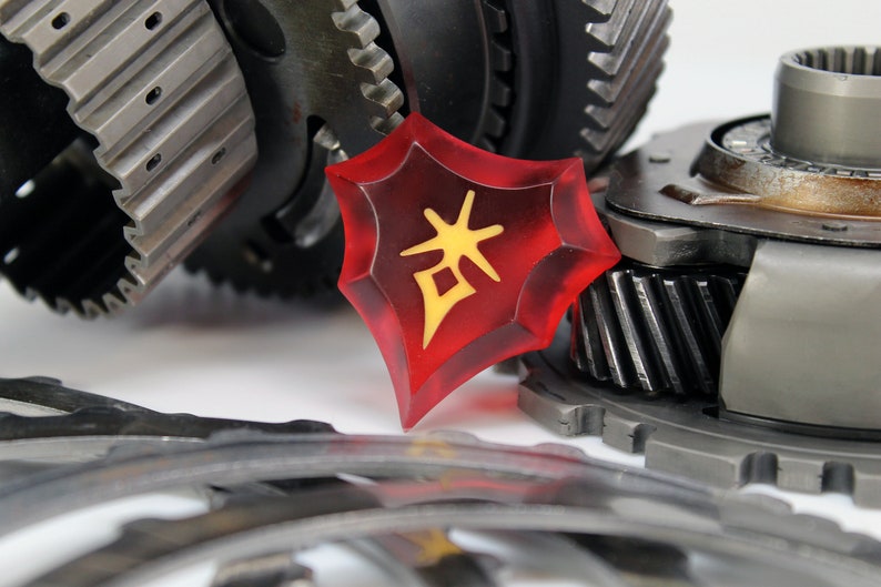 May include: A red, star-shaped, plastic token with a yellow Chinese character on it. The token is lying on a pile of metal gears.