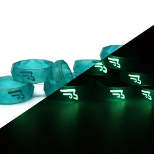 May include: A group of teal blue silicone rings with a black logo on them. The rings glow green in the dark.