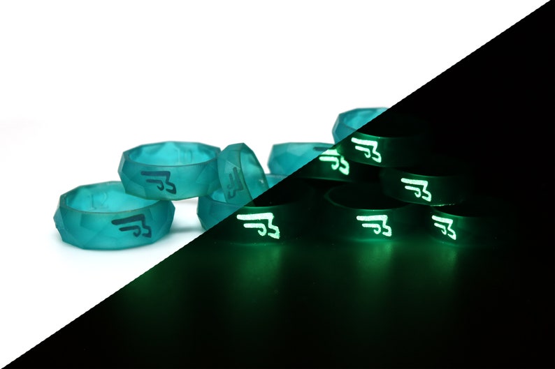 May include: A group of teal blue silicone rings with a black logo on them. The rings glow green in the dark.