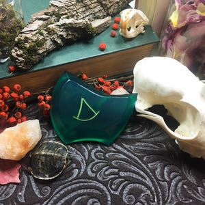May include: A green resin pendant with a stylized letter D in the center. The pendant is on a dark patterned surface with a small turtle and a piece of orange rock.