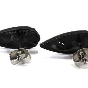 May include: A pair of black stud earrings with a pointed, teardrop-shaped design. The earrings have silver posts and backs.