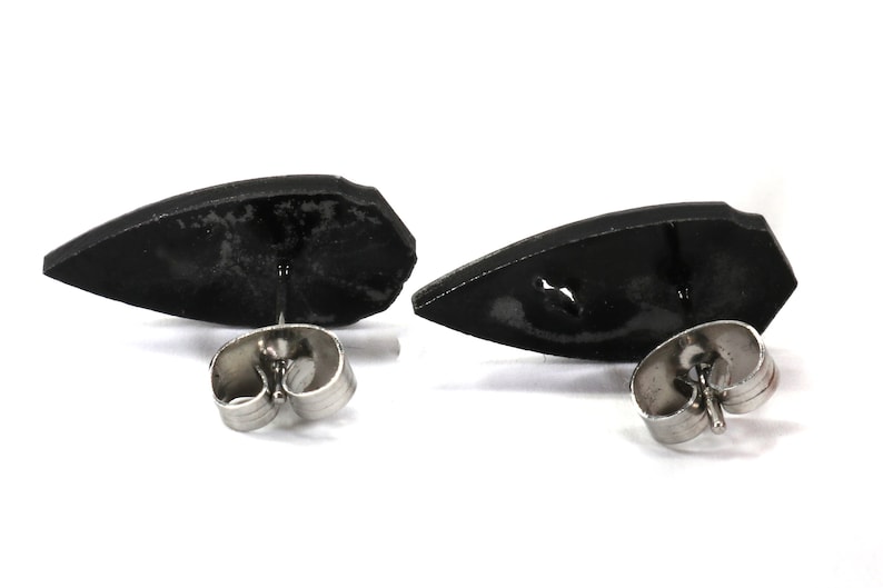 May include: A pair of black stud earrings with a pointed, teardrop-shaped design. The earrings have silver posts and backs.