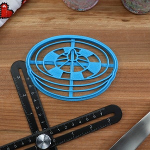 May include: A blue plastic circular cookie cutter with a concentric circle design. The cutter is on a wooden surface.
