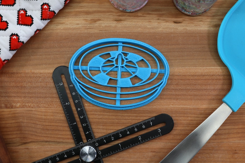 May include: A blue plastic circular cookie cutter with a concentric circle design. The cutter is on a wooden surface.