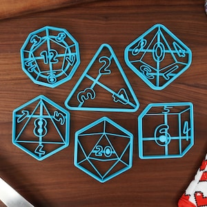 May include: Set of six blue plastic cookie cutters shaped like dice with numbers 4, 6, 8, 12, 20, and a triangle with the numbers 2, 3, and 4.