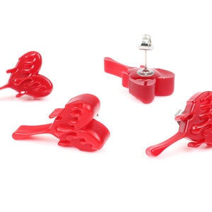 May include: Three pairs of red heart-shaped earrings with a flame design. The earrings are made of resin and have a silver post.