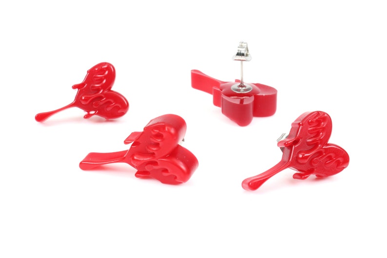 May include: Three pairs of red heart-shaped earrings with a flame design. The earrings are made of resin and have a silver post.