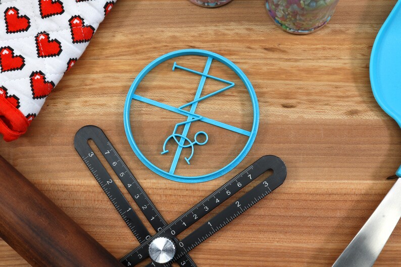May include: A blue plastic cookie cutter shaped like a stick figure doing a handstand. The cookie cutter is on a wooden surface.