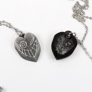 May include: Two silver heart-shaped pendants on chains. One pendant has a detailed design of a target with lines radiating out. The other pendant is black and has a textured surface.