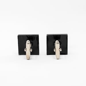 May include: A pair of black square cufflinks with silver-toned metal clasps.