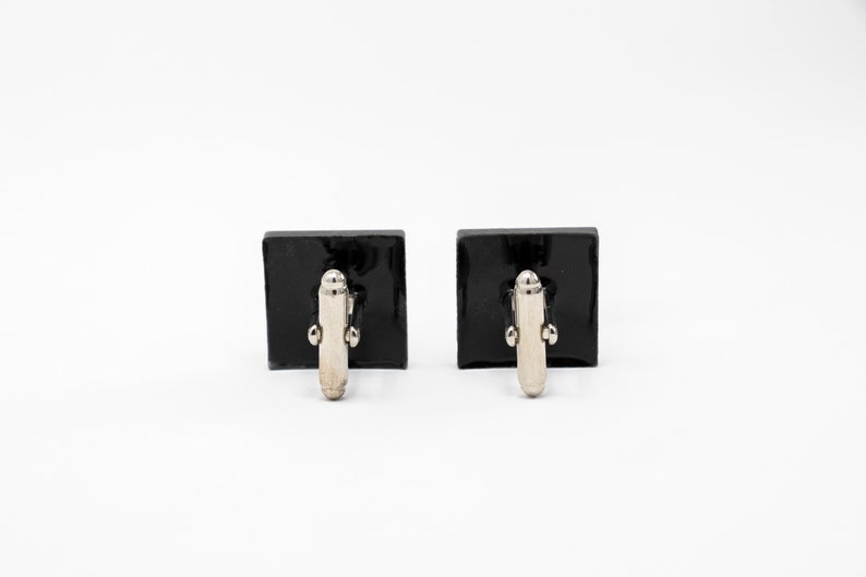 May include: A pair of black square cufflinks with silver-toned metal clasps.