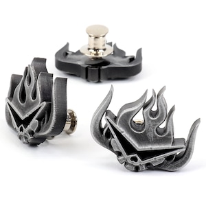 Puede incluir: Tres pines de metal de color plateado con un diseño de llama y una calavera en el centro. Los pines tienen un cierre de poste.