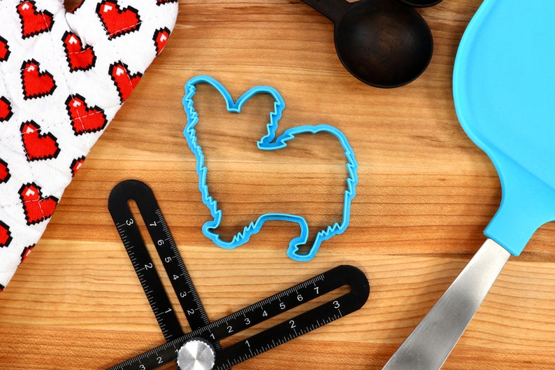 May include: Blue plastic cookie cutter shaped like a Papillon dog on a wooden surface.