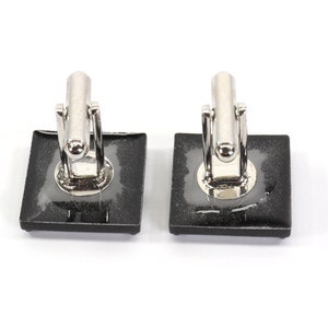 May include: A pair of silver cufflinks with black square-shaped settings. The cufflinks are on a white background.