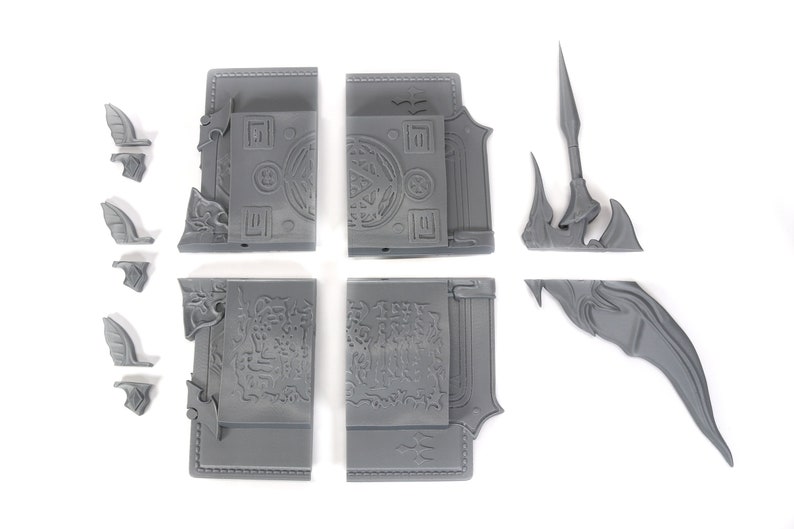 May include: A set of gray plastic pieces for a miniature model. The pieces include a book with intricate details, a spear, and a wing.