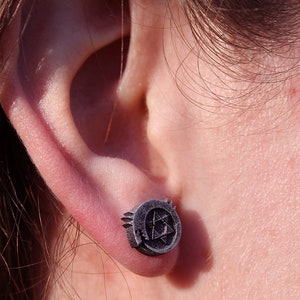 May include: A pair of silver stud earrings featuring a stylized triangular design. The earrings are worn in the earlobe.