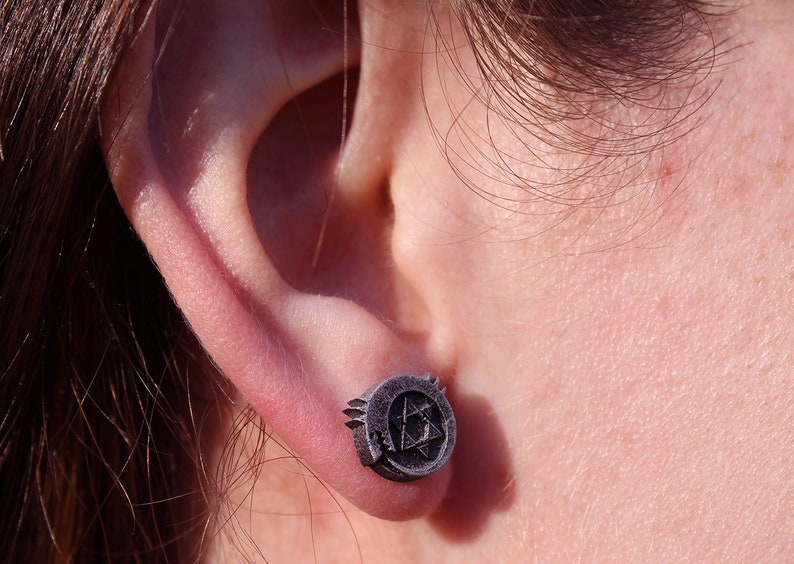May include: A pair of silver stud earrings featuring a stylized triangular design. The earrings are worn in the earlobe.