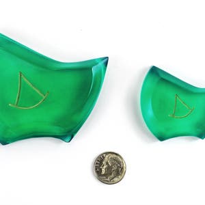 May include: Two green glass dishes with a gold sailboat design. The larger dish is about 5 inches wide and the smaller dish is about 3 inches wide.