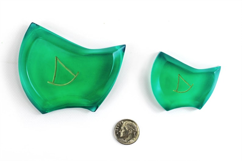 May include: Two green glass dishes with a gold sailboat design. The larger dish is about 5 inches wide and the smaller dish is about 3 inches wide.