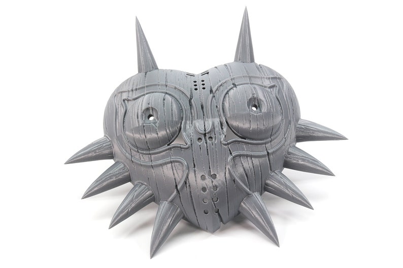 May include: A gray 3D printed mask shaped like a heart with spikes around the edges. The mask has two large eye holes and a smaller hole in the center.