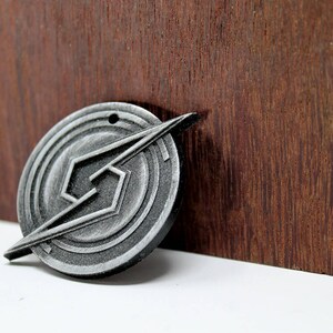 May include: A silver metal pendant with a geometric design. The pendant features a stylized lightning bolt shape within a circular frame.