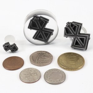 May include: A set of four black metal stamps with a geometric design. The stamps are different sizes and are displayed on a white surface with coins.