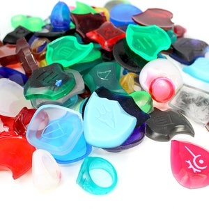 Puede incluir: Una colecci&oacute;n de piezas de juego de pl&aacute;stico de colores, transl&uacute;cidas y opacas. Las piezas tienen forma de escudos, anillos y l&aacute;grimas. Algunas de las piezas tienen s&iacute;mbolos o dise&ntilde;os.