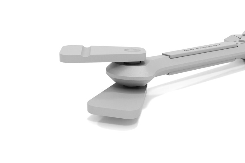 May include: A light gray, mechanical device with a pivoting arm and a rectangular base. The device has a smooth, matte finish and appears to be made of plastic or a similar material. The design is modern and minimalist.
