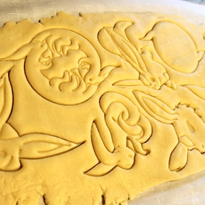 May include: A sheet of yellow cookie dough with bunny and moon shapes cut out using cookie cutters.