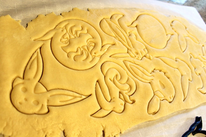 May include: A sheet of yellow cookie dough with bunny and moon shapes cut out using cookie cutters.
